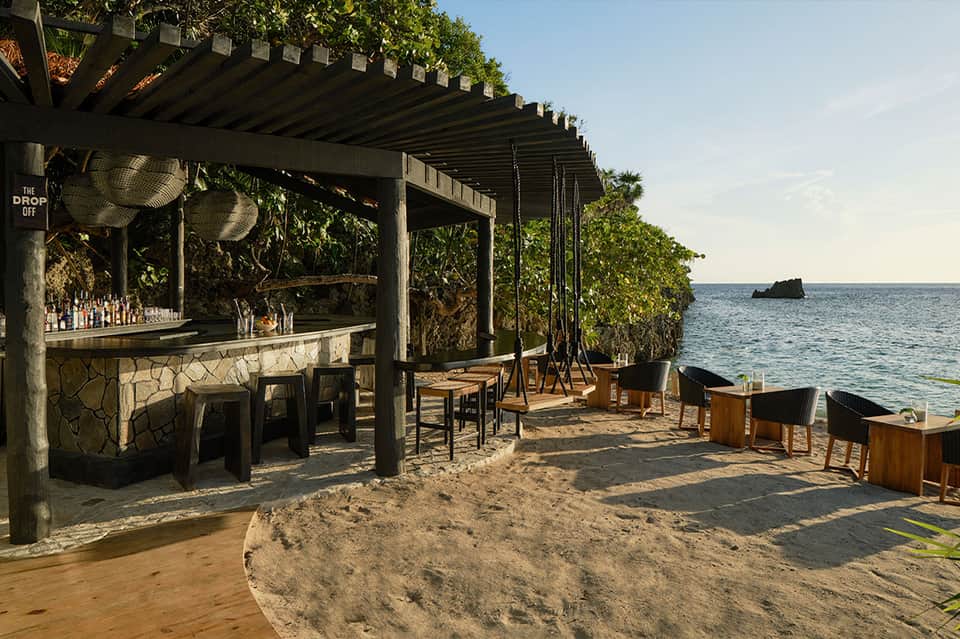 Beach bar with stone counter, wooden furniture, and ocean view with mangrove trees