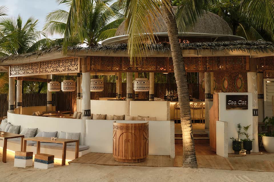 Beachfront tiki bar with thatched roof, white walls, wooden accents, and palm trees