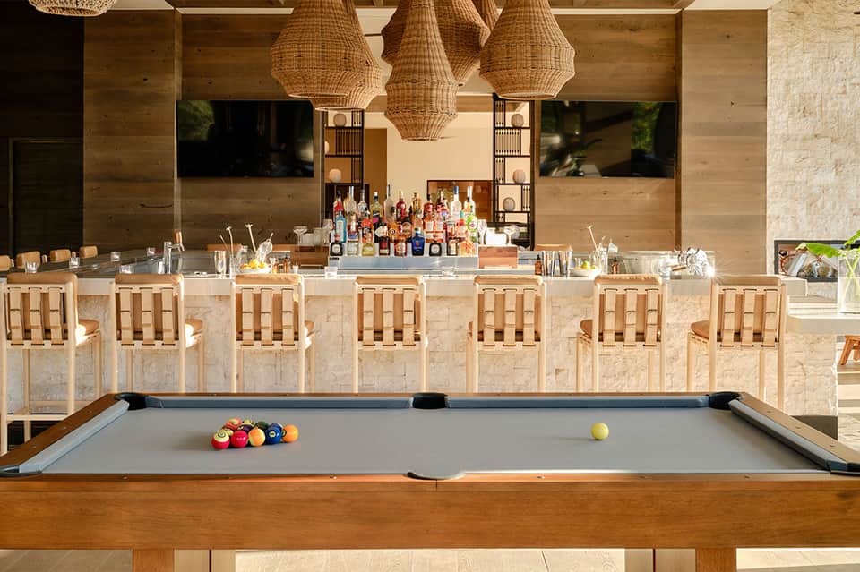 Modern bar and lounge with pool table, woven pendant lights, stone bar counter, and wall-mounted televisions
