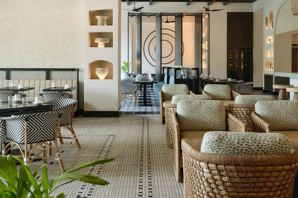 Upscale hotel lobby with geometric patterned floor, woven lounge chairs, and decorative wall niches