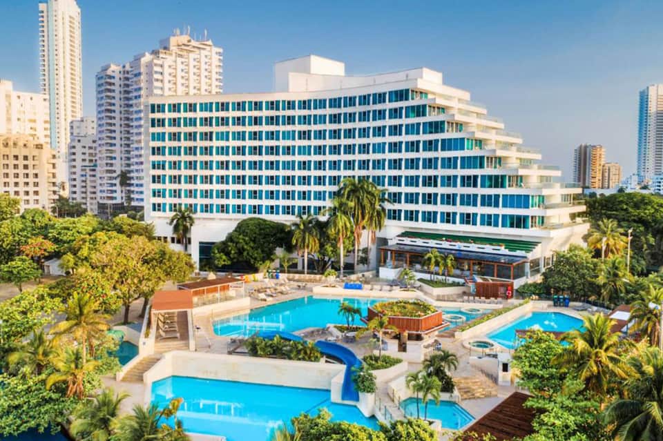 Aerial view of beachfront resort with turquoise pools, tropical landscaping, and multi-story hotel building