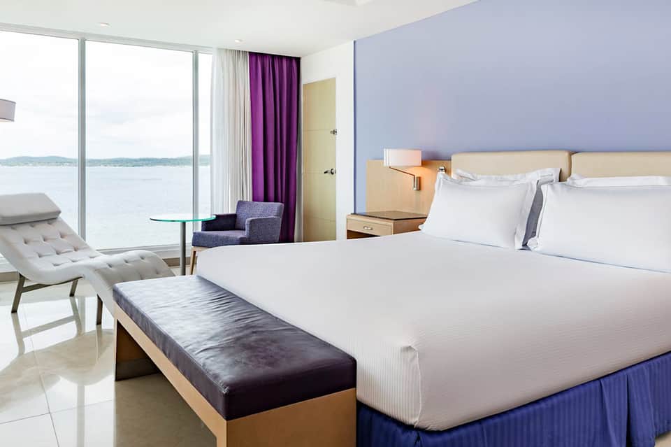 Modern beachfront hotel room with king bed, ocean view balcony, and contemporary furnishings