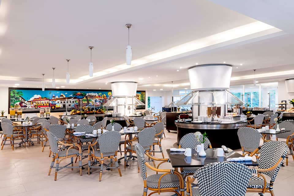 Modern hotel dining area with checkered chairs, pendant lights, and colorful carnival-themed artwork on walls