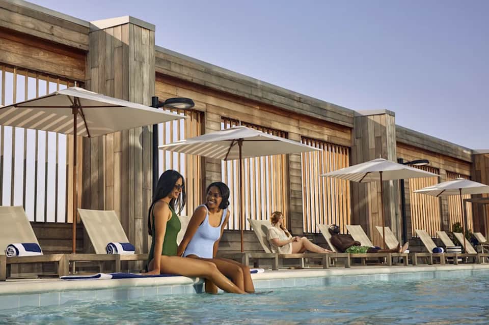 Modern pool area with wooden cabanas, umbrellas, and guests enjoying water at luxury resort