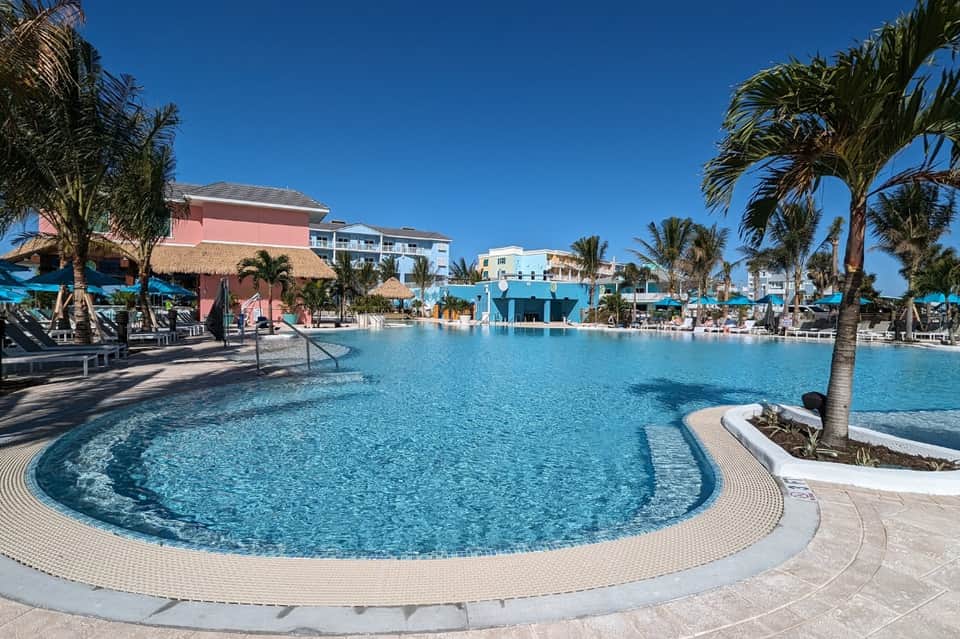 Resort pool area with turquoise water, palm trees, and pastel-colored buildings