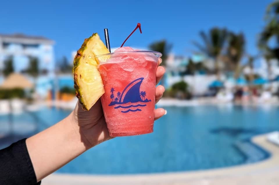 Tropical cocktail with pineapple garnish held poolside with resort in blurred background