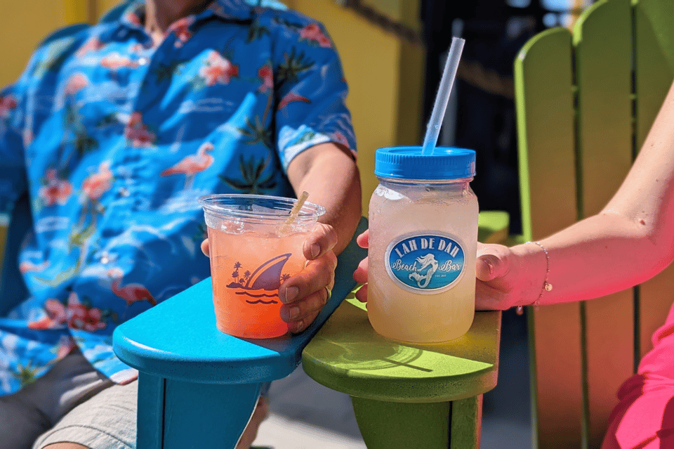 Two colorful tropical cocktails served in beach bar cups at outdoor seating area