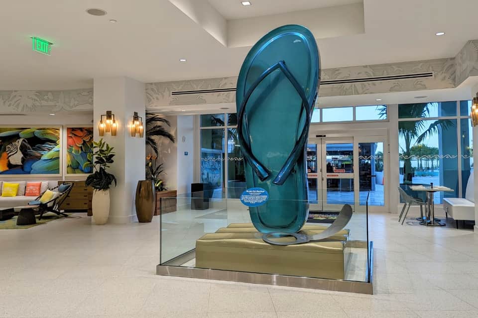 Modern hotel lobby with large blue glass flip-flop sculpture and ocean view through floor-to-ceiling windows