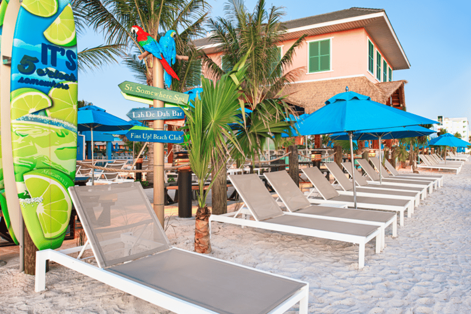 Colorful beach club with blue umbrellas, lounge chairs, palm trees, and tropical themed signage