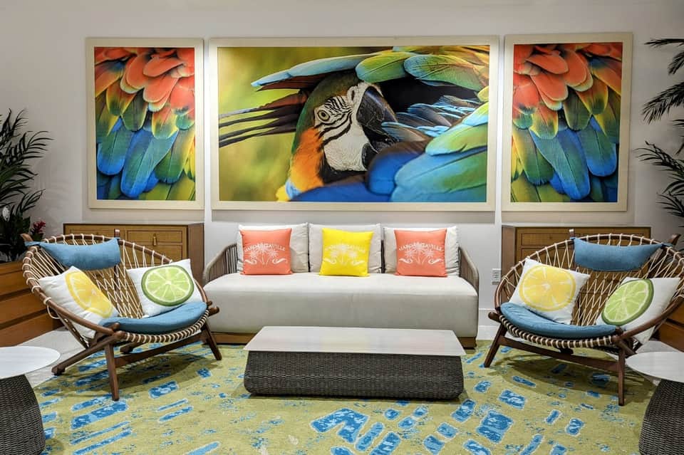 Modern lounge with colorful macaw artwork, woven chairs with fruit-patterned pillows, and white sofa
