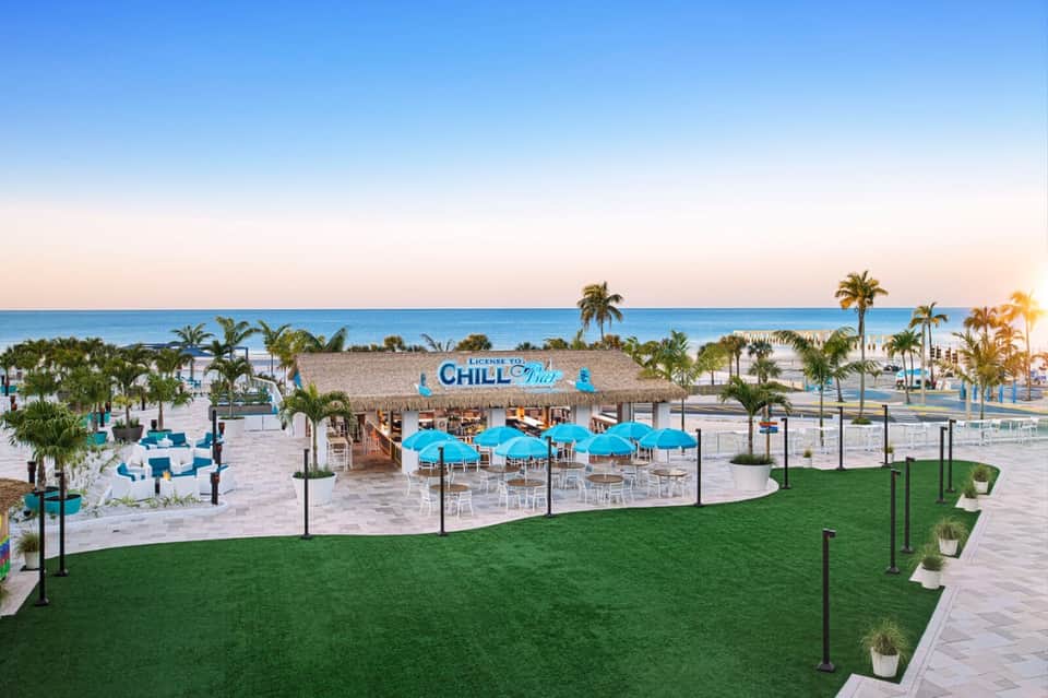 Beachfront Chill Pad bar with blue umbrellas, thatched roof, and ocean view at sunset