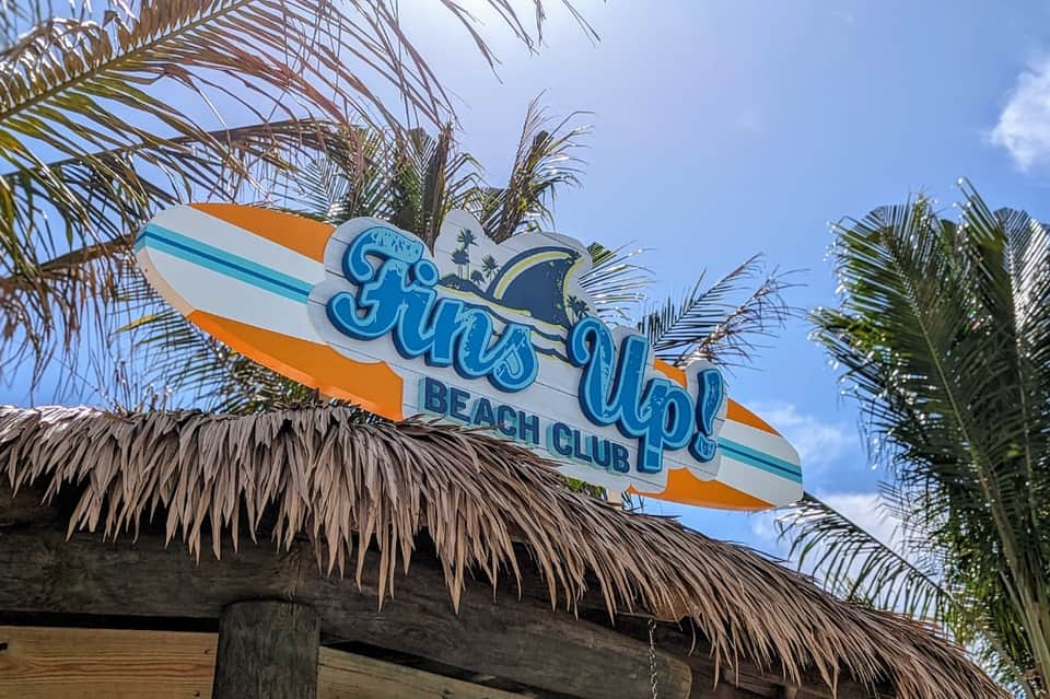Sun Up Beach Club sign with surfboard design under palm trees