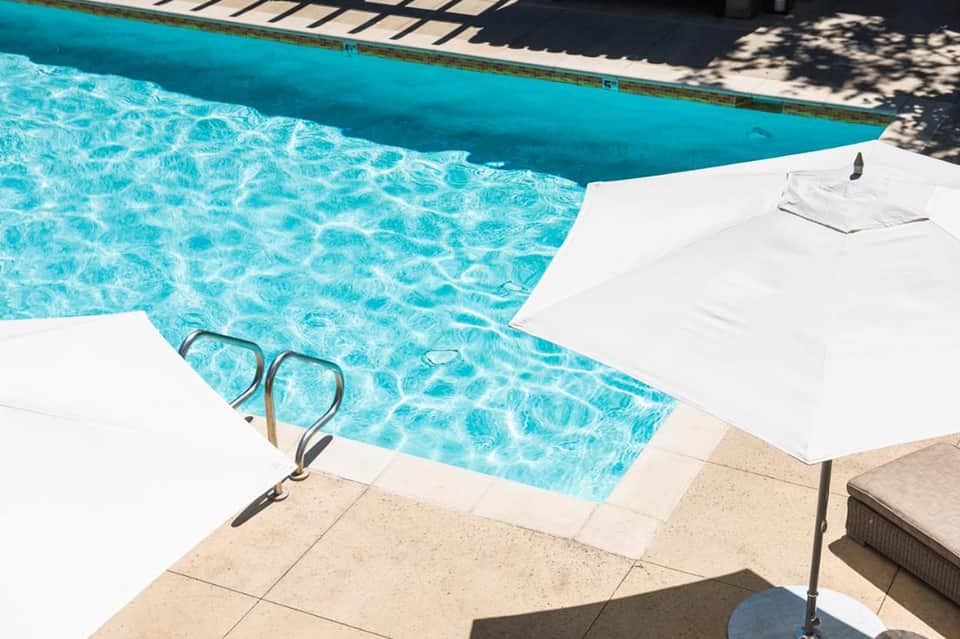 Turquoise pool corner with white lounger and metal handrails on concrete deck