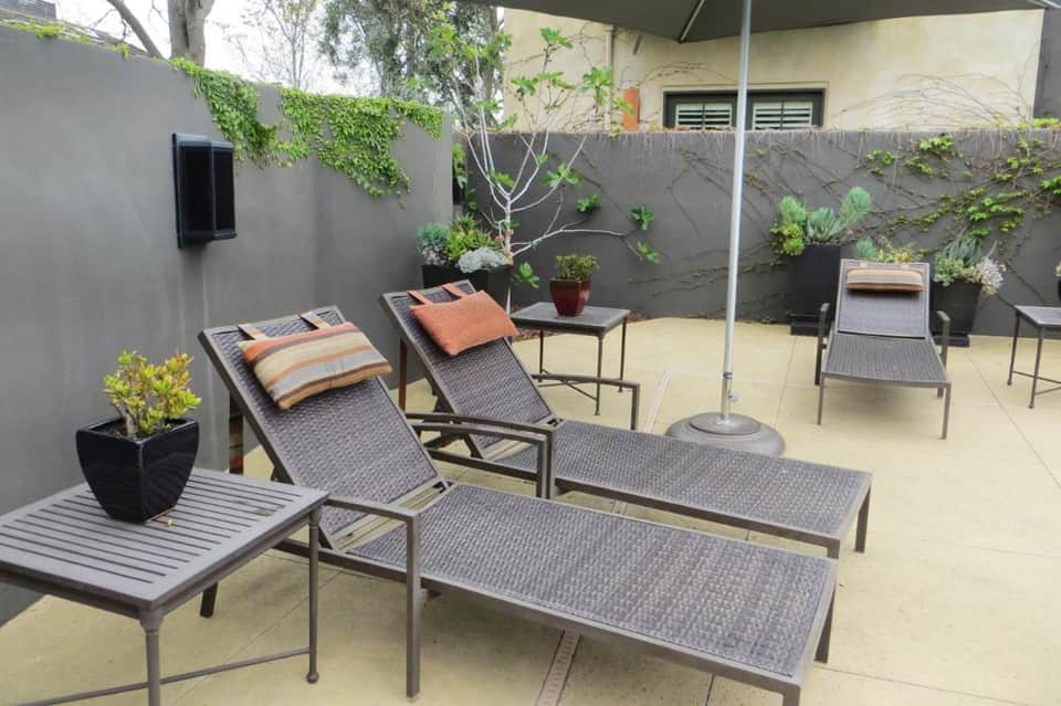 Outdoor courtyard with lounge chairs, umbrella, potted plants, and ivy-covered gray walls