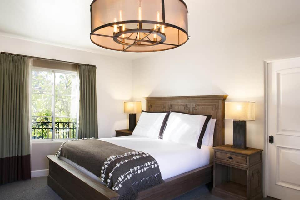 Elegant bedroom with wooden bed frame, white bedding, pendant lighting, and balcony with curtains
