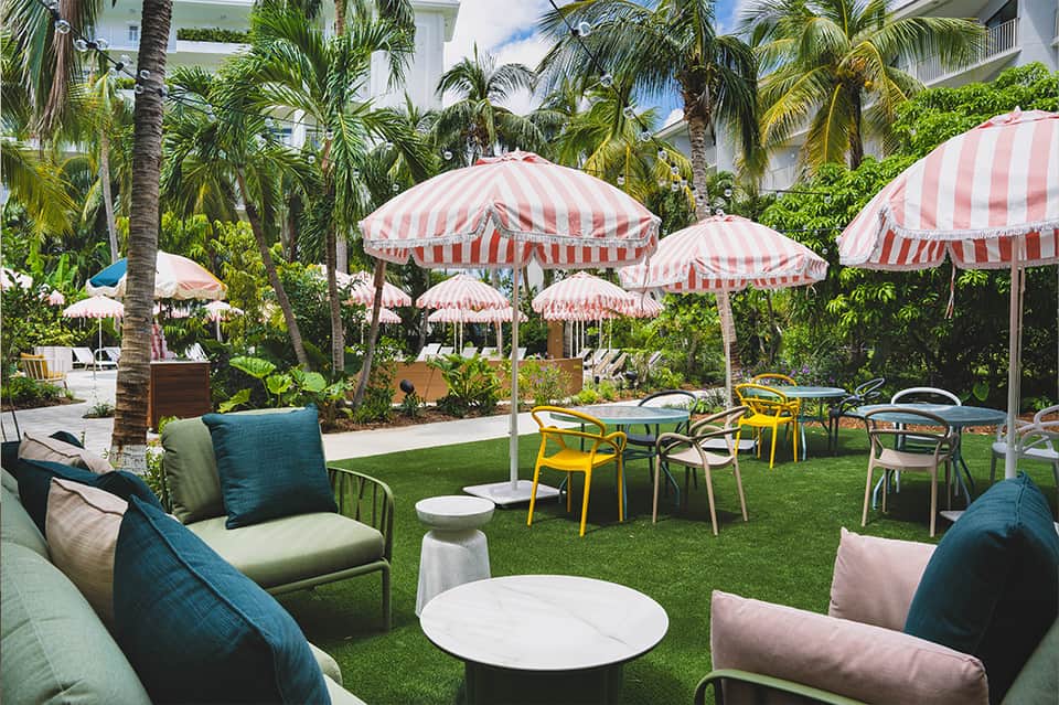 Tropical garden lawn with striped pink and white umbrellas, colorful chairs, and palm trees