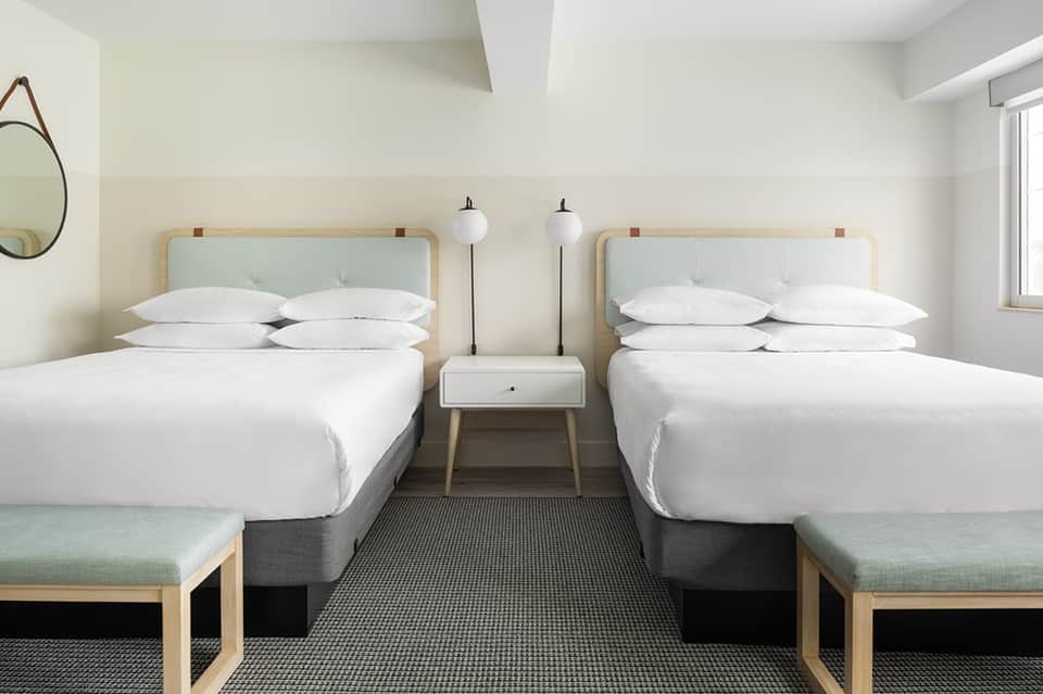 Modern hotel room with two queen beds, natural wood headboards, and minimalist decor