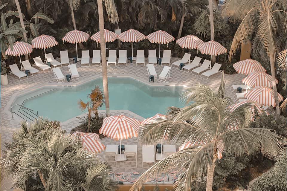 Overhead view of resort pool surrounded by striped umbrellas, lounge chairs, and palm trees