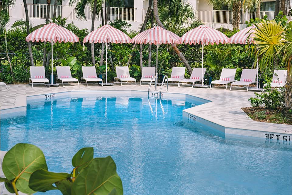 Resort pool with pink and white striped umbrellas, white lounge chairs, and tropical landscaping in background