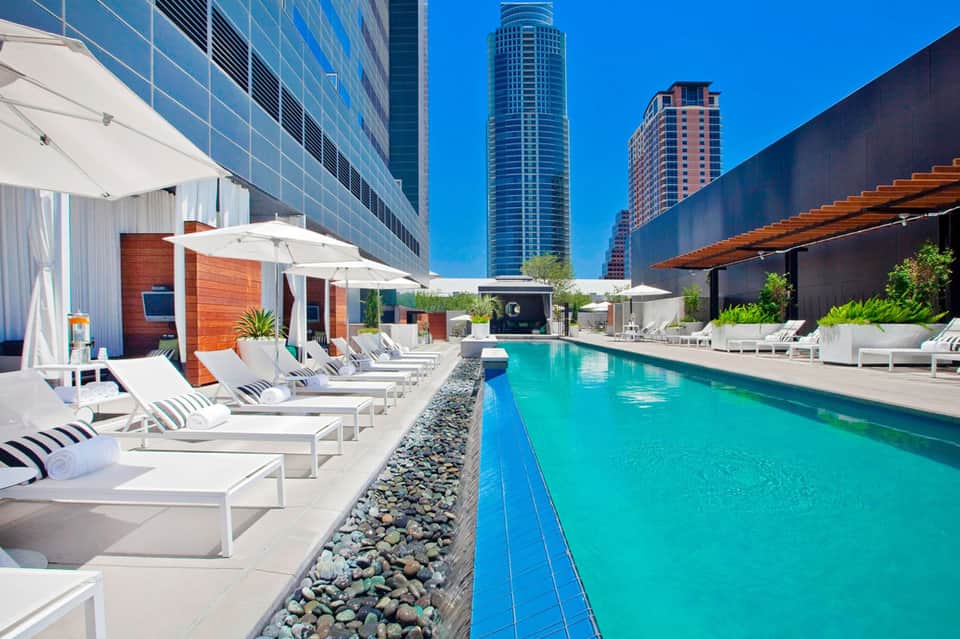 Modern rooftop pool with turquoise water, white loungers, and tall buildings in urban downtown setting