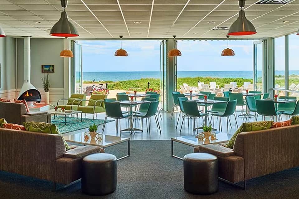 Beachfront lounge with floor-to-ceiling windows overlooking ocean, green seating, and copper pendant lights