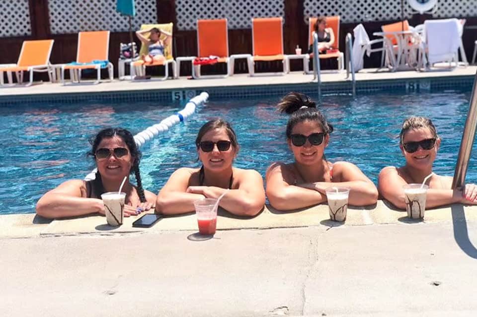 Four women relaxing poolside with drinks at a resort swimming pool