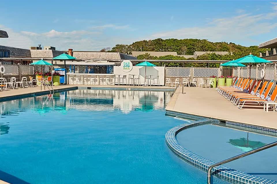 Resort pool with turquoise water, colorful lounge chairs, teal umbrellas, and white building structures
