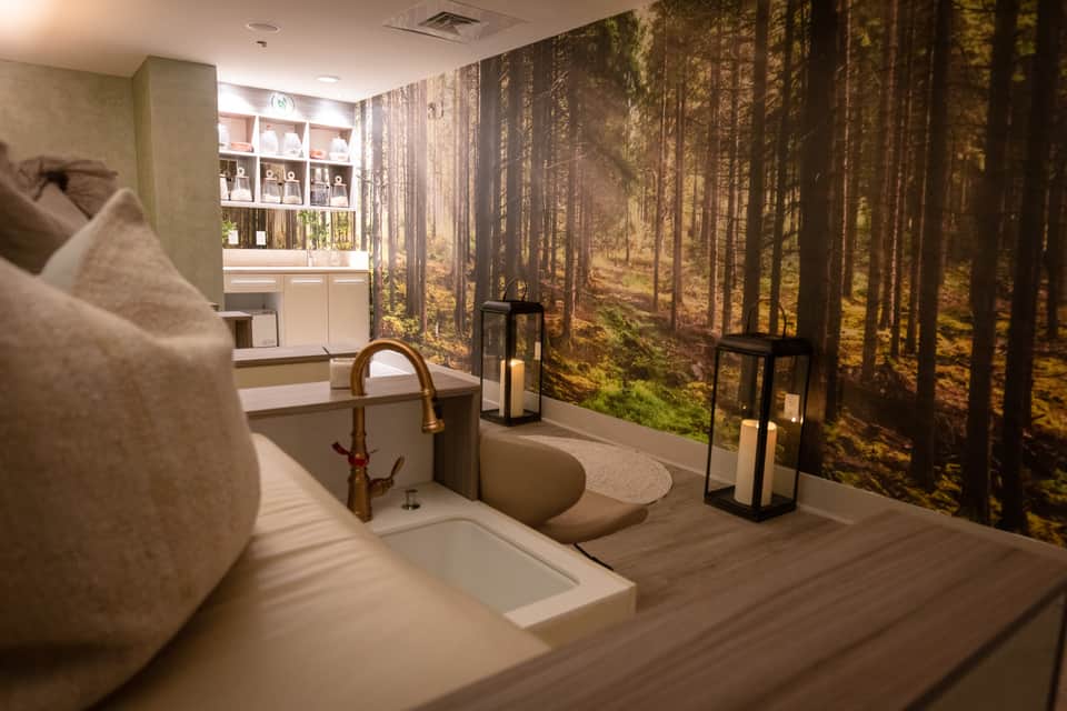 Luxury spa bathroom with soaking tub, forest mural wallpaper, and white shelving unit
