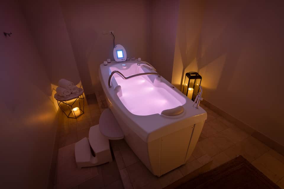 Spa treatment room with illuminated pink hydrotherapy tub, ambient lighting, and folded towels on side table