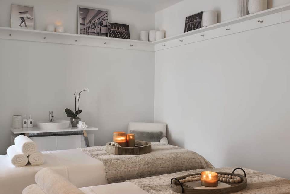Serene spa treatment room with white linens, massage table, candles, and sink vanity