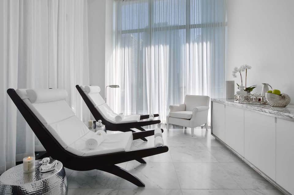 Modern spa relaxation room with white loungers, minimalist furniture, and sheer white curtains