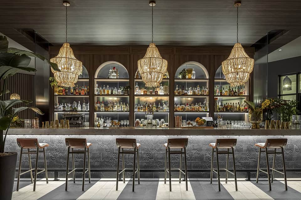 Upscale bar with gold pendant lights, dark shelving displaying spirits, and leather bar stools