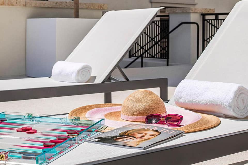 Poolside loungers with straw hat, sunglasses, and rolled towels on table