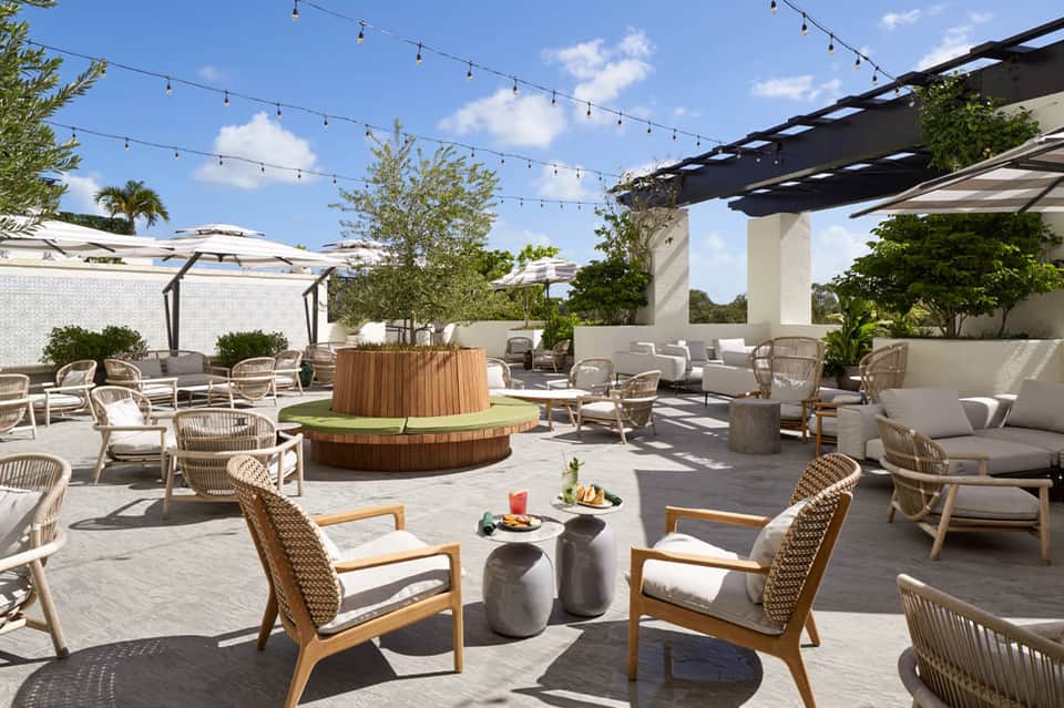Rooftop lounge with fire pit, string lights, wooden pergola, lounge seating, and woven accent chairs