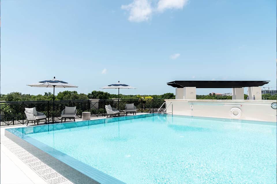 Rooftop pool with lounge chairs, umbrellas, and city skyline view on clear day