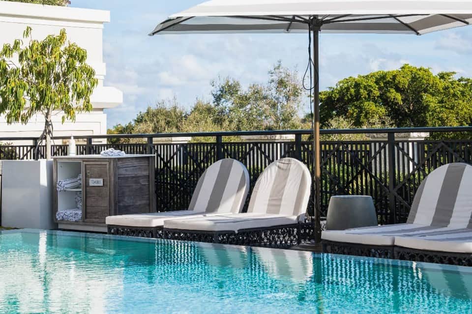 Luxury poolside lounge area with white umbrellas and striped loungers overlooking turquoise water