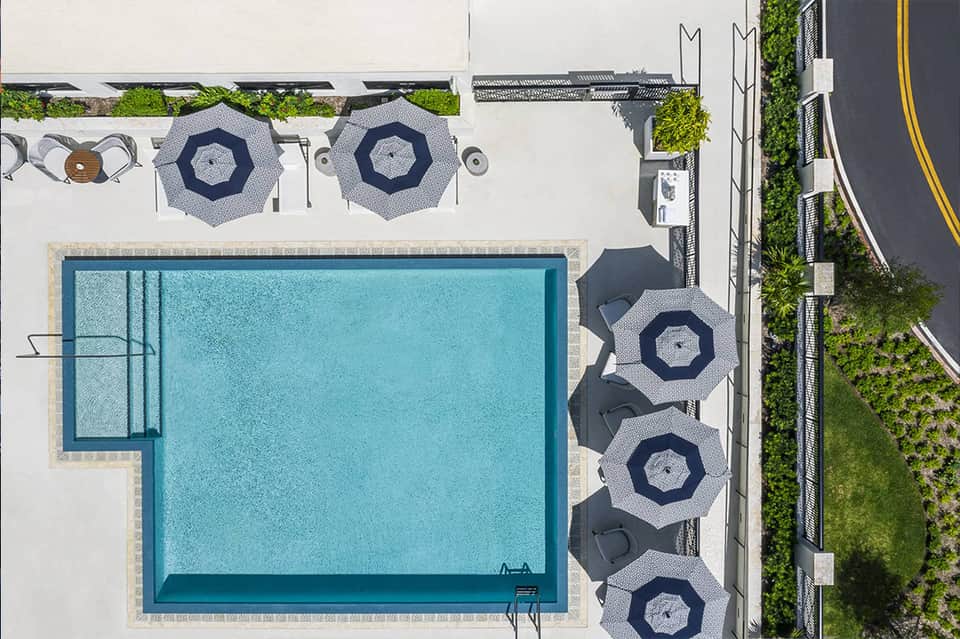 Overhead view of rectangular pool with navy hexagonal umbrellas and lounge chairs on white patio