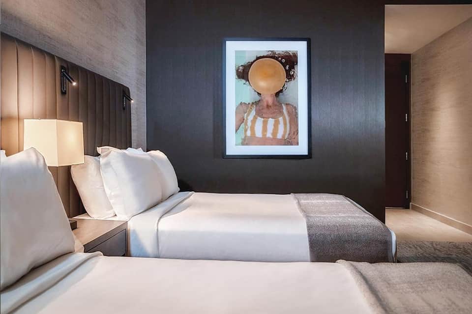 Modern hotel bedroom with two beds, dark accent wall, and framed artwork