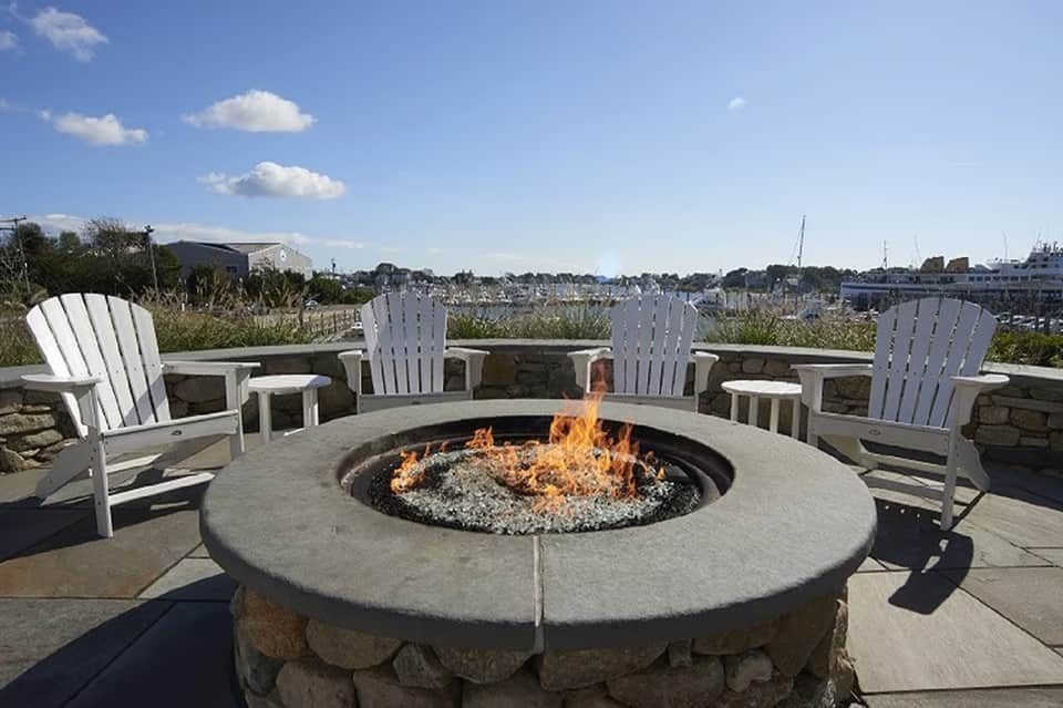 Outdoor fire pit seating area with white Adirondack chairs overlooking marina and sailboats on water
