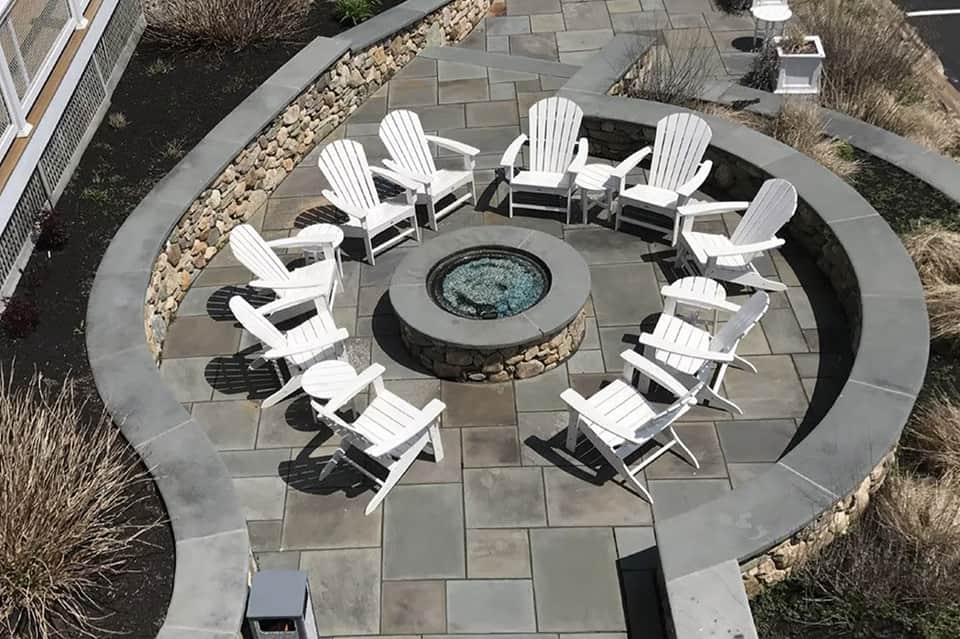 Overhead view of circular fire pit seating area with white Adirondack chairs on stone patio