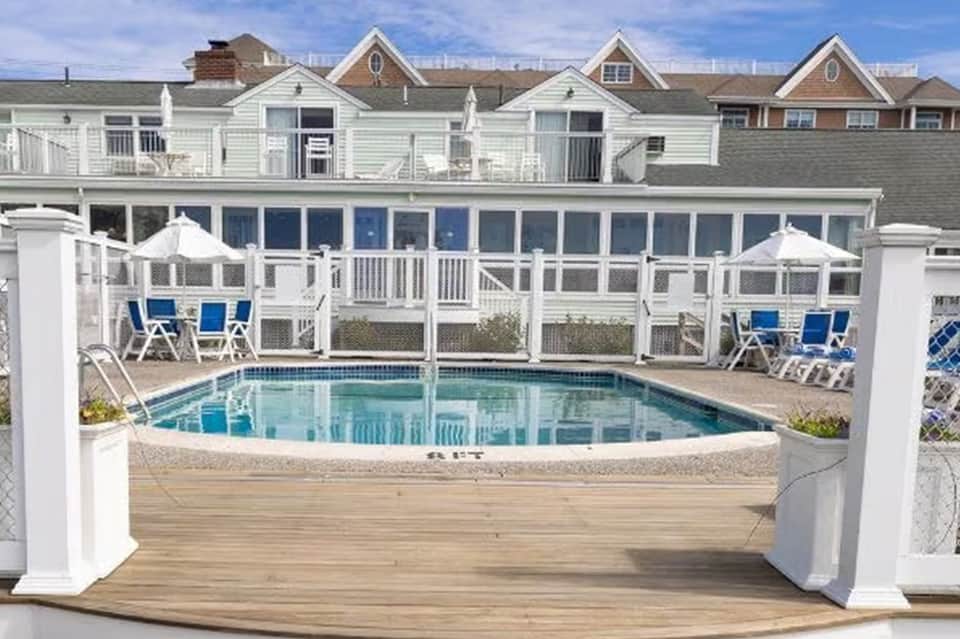 Beachfront resort pool enclosed by white fence with blue umbrellas and buildings