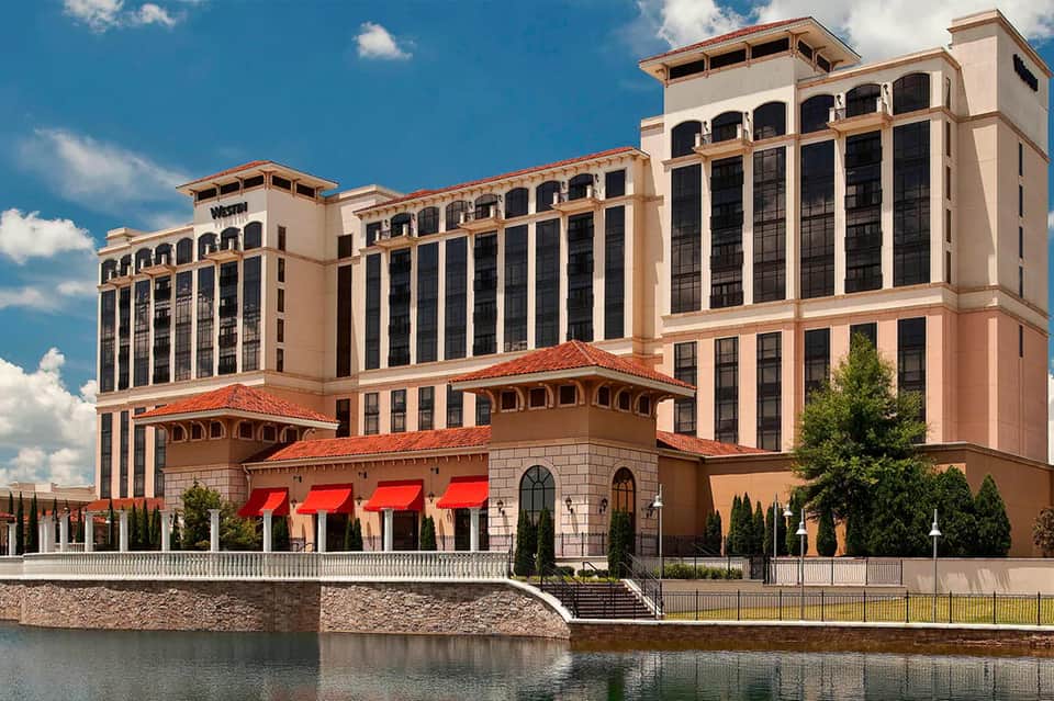 Waterfront hotel with terracotta roofing, arched colonnade, red awnings, and riverside promenade