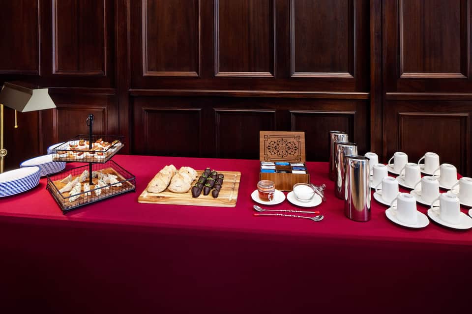 Elegant buffet spread with pastries, bread, olives, coffee cups on red tablecloth