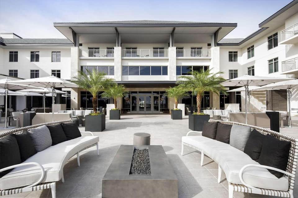 Modern hotel courtyard with fire pit seating, palm trees, and contemporary architecture