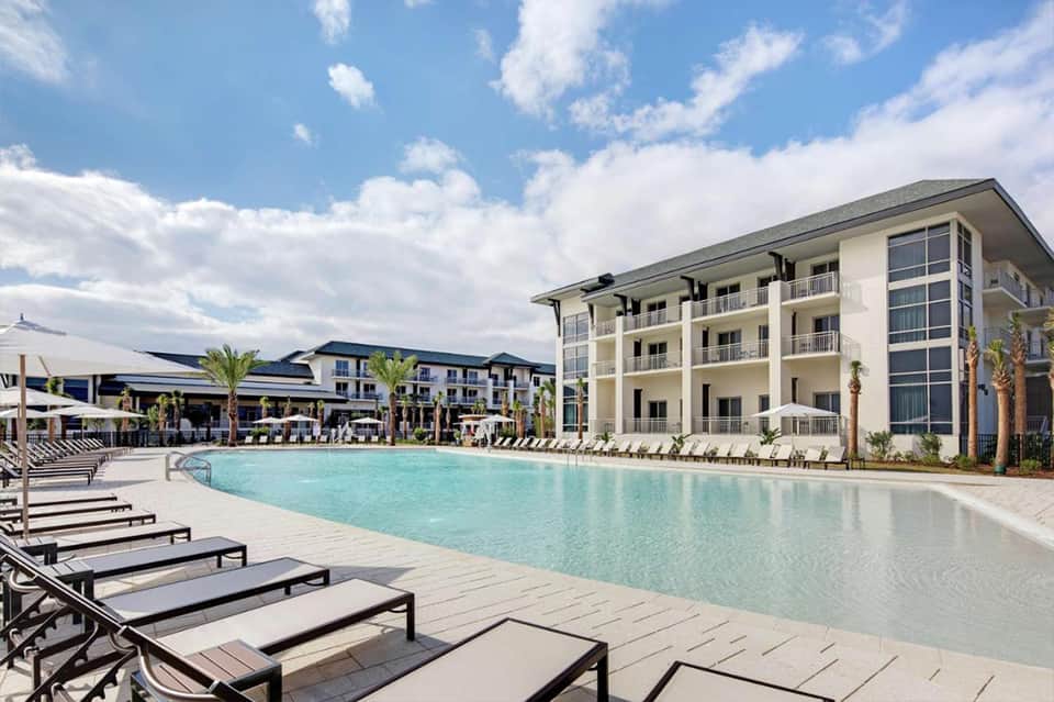 Resort pool with lounge chairs and white umbrellas, multi-story hotel building in background