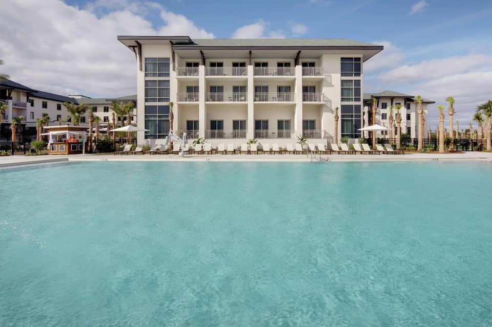 Beachfront resort building with white architecture and palm trees beside turquoise pool