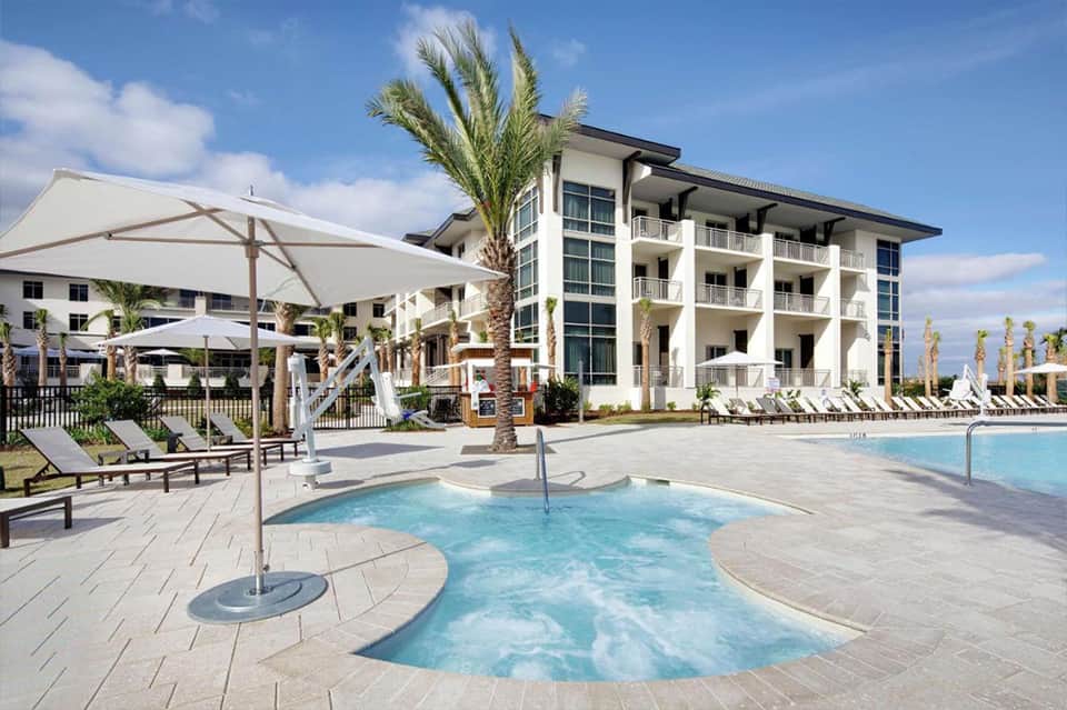 Beachfront resort with pool, spa area, palm trees, and multi-story white building