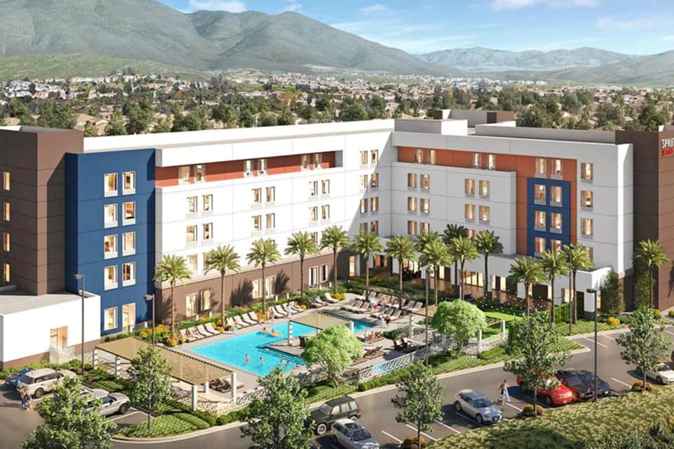 Contemporary hotel exterior with blue and white facade, swimming pool, and mountain backdrop in desert landscape