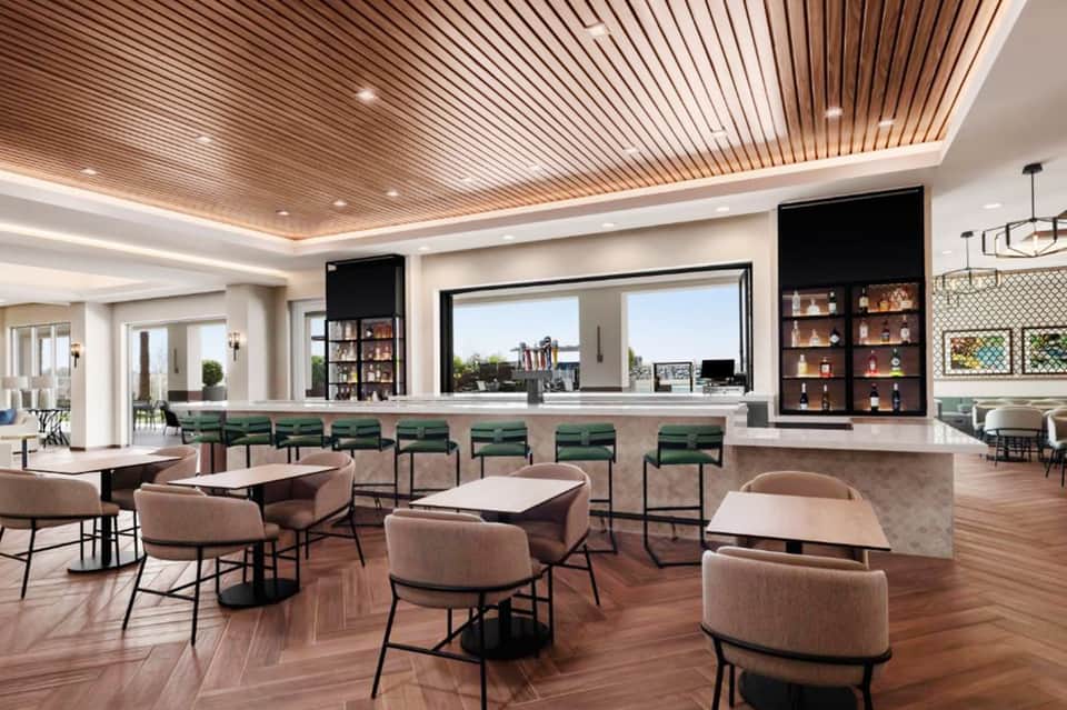 Modern hotel bar and lounge with wooden ceiling, green bar stools, and expansive window views