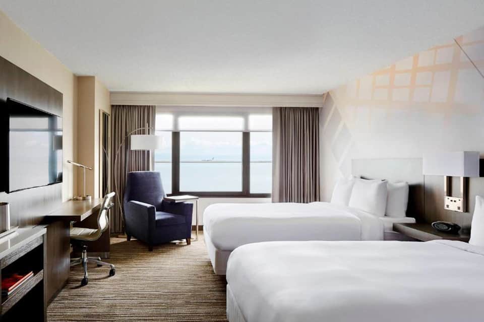 Luxury hotel room with two queen beds, ocean view windows, work desk, and contemporary furnishings